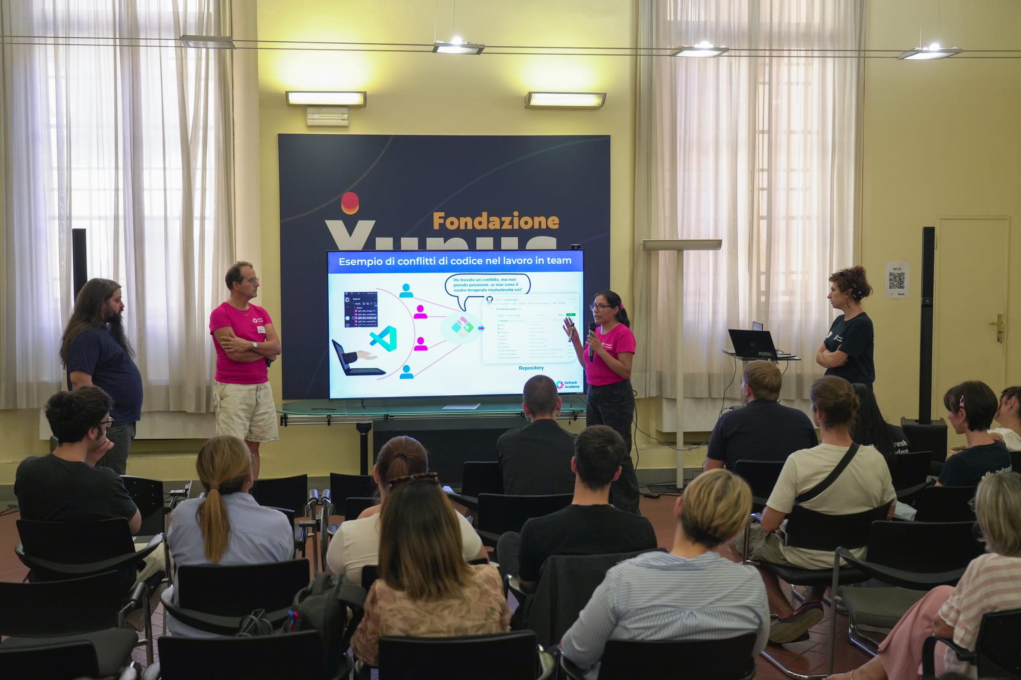 Un gruppo di studenti presenta il proprio progetto con una slide sui conflitti di codice nel lavoro in team