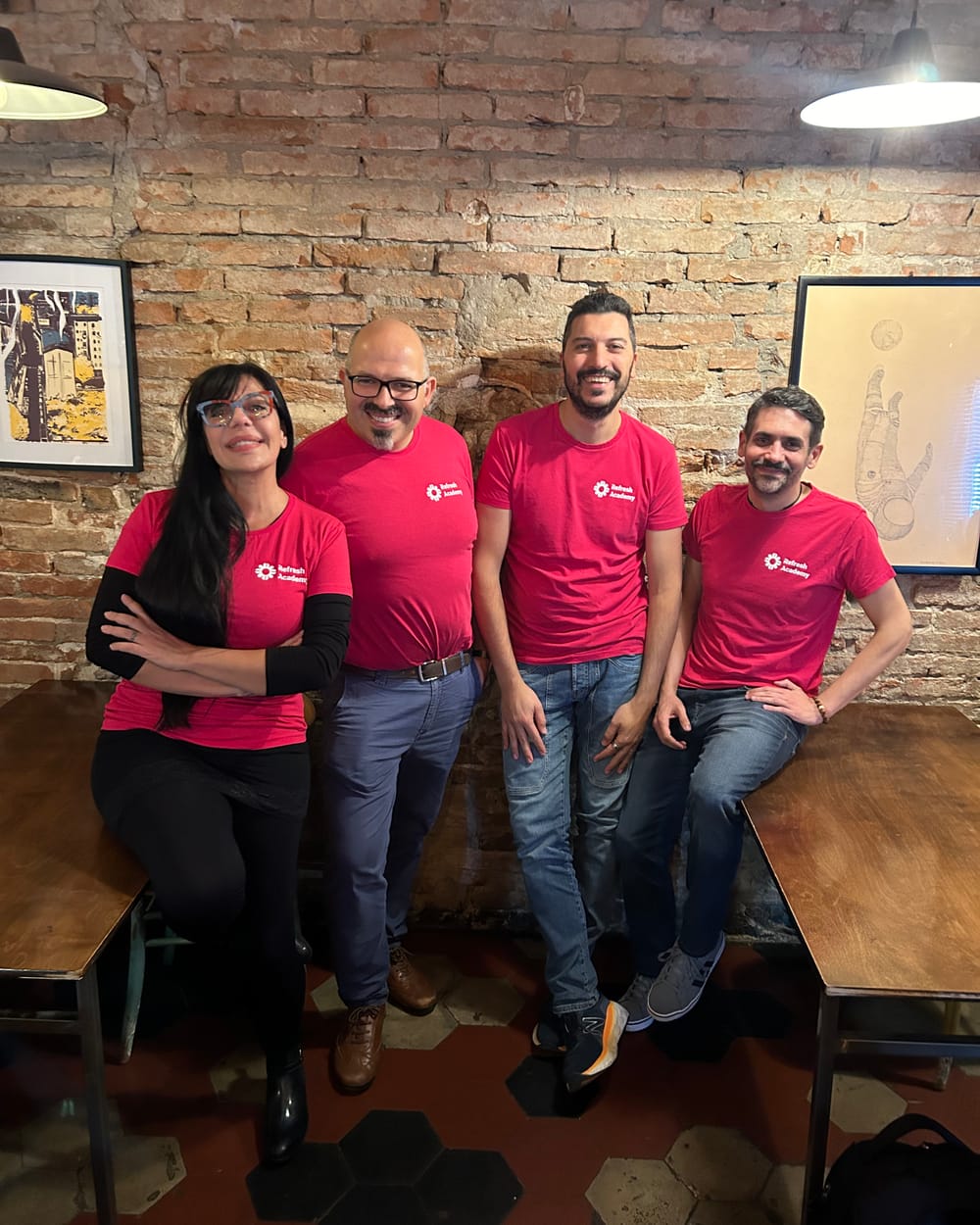 Quattro persone del team di Refresh Academy con la maglietta rossa, sorridenti davanti a un muro di mattoni