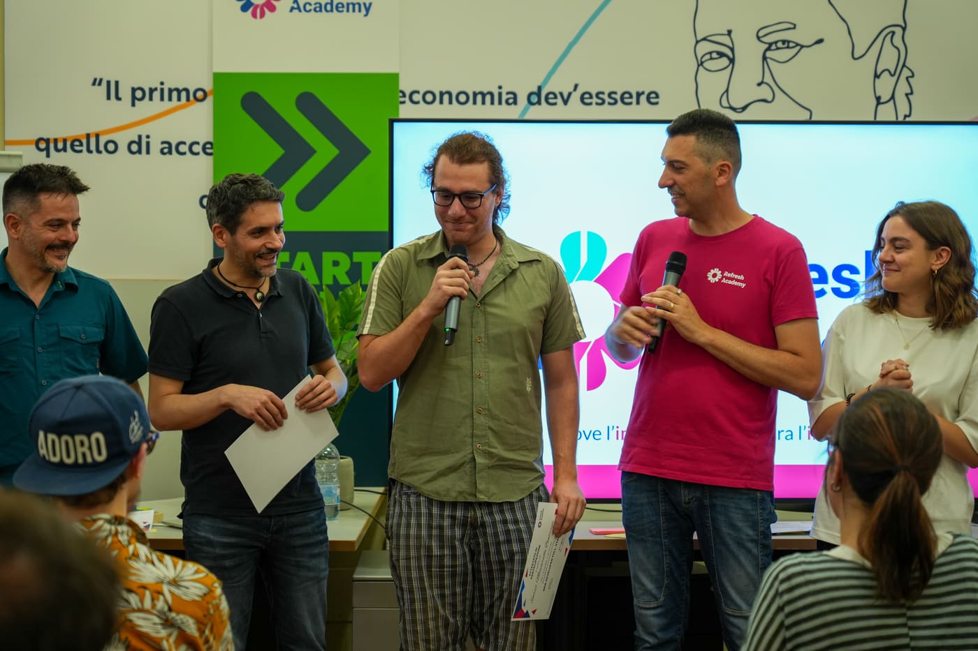 Durante una consegna di attestati, due persone parlano al microfono davanti allo schermo con il logo di Refresh Academy