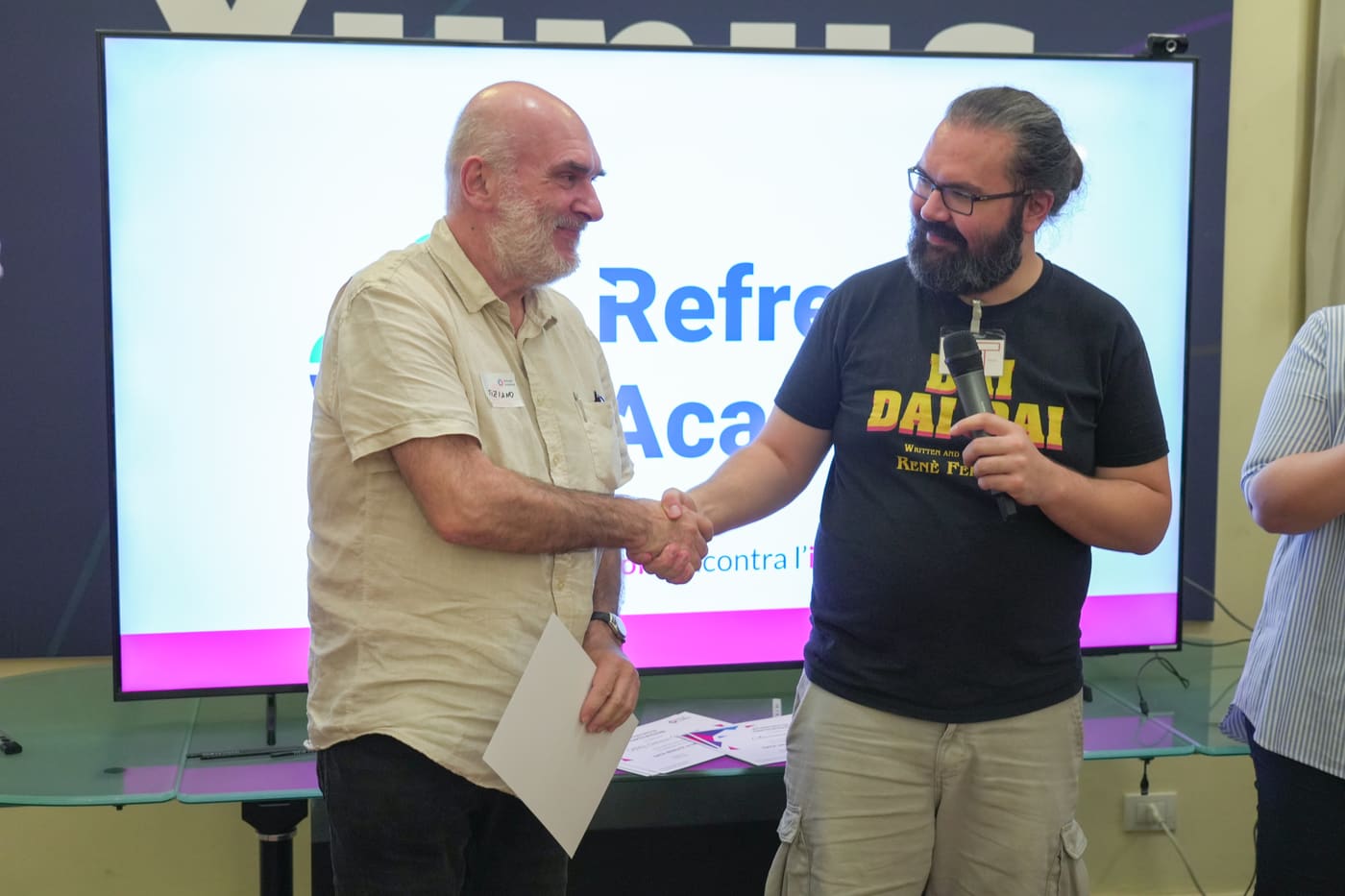Una stretta di mano durante la consegna di un attestato, davanti allo schermo con il logo di Refresh Academy